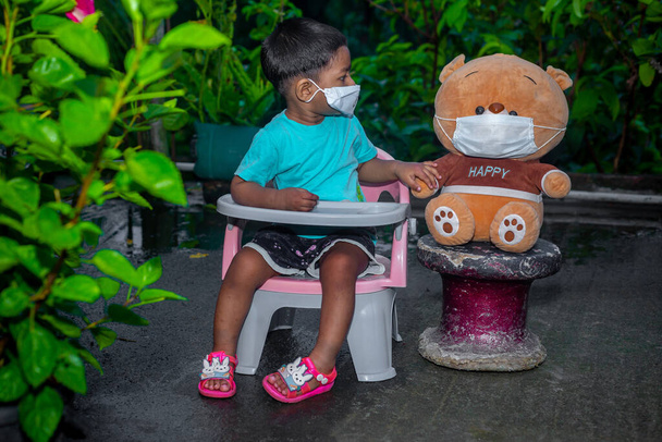 Lapsi ja nukke istuvat puutarhassa naamioituneina sepelvaltimoviruksen pandemiaan.. - Valokuva, kuva