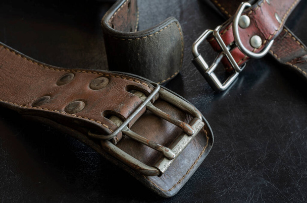 Fragment of two old genuine leather collars on a dark table. Cracked shabby leather and metal fittings. Real vintage dog collars. Love to the animals. Selective focus. - Valokuva, kuva