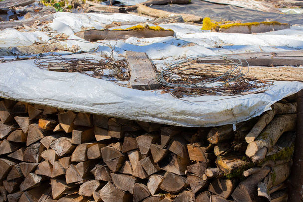 Gehakt brandhout gestapeld met een dekzeil met prikkeldraad erop om het tegen de regen te beschermen en droog te houden - Foto, afbeelding