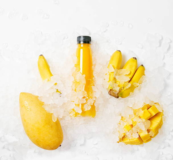 Flat lay top view colorful yellow juice bottle with bananas and mango in ice. Healthy lifestyle concept. Vegan, vegetarian food - Фото, зображення