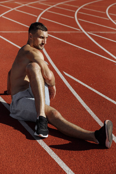 Man sitting on the track and stretching after workout. Sportsman. Strong man - Photo, Image