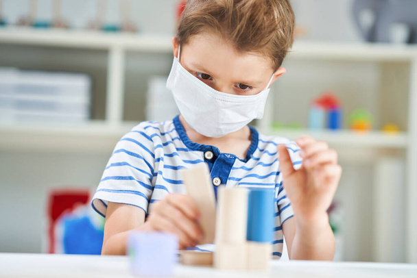 Adorable niño en el jardín de infantes con máscara debido a la pandemia de coronavirus
 - Foto, imagen