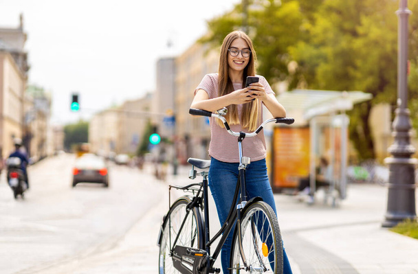 Attractive young woman using smartphone while out cycling through the city - Zdjęcie, obraz