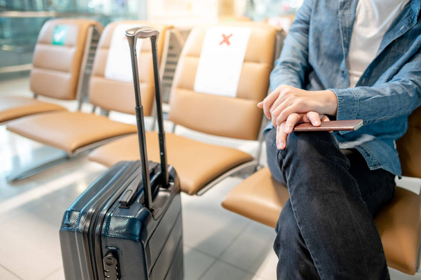 Wyjazd za granicę. mężczyzna turysta ręka posiadający paszport siedzi z walizką bagażu na siedzeniu w poczekalni terminalu lotniska. - Zdjęcie, obraz
