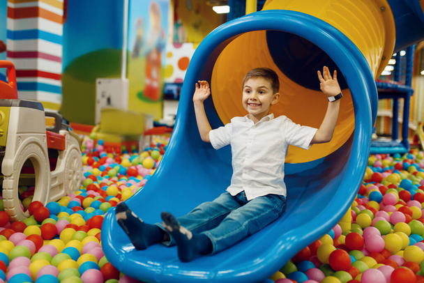 Маленький мальчик скачет с холма в развлекательный центр. Мужской детский отдых на праздники, детское счастье, счастливый ребенок на детской площадке
 - Фото, изображение