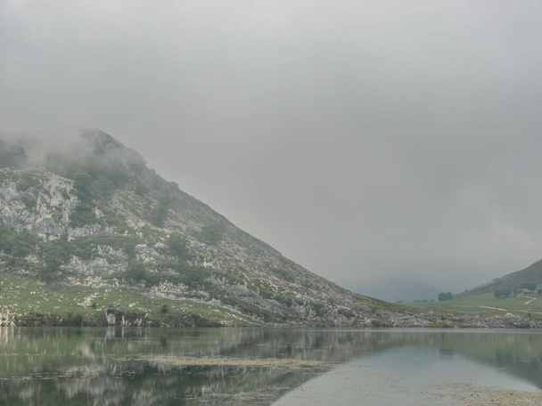 Jezero odrážející okolní hory. Je zataženo a všechno je obklopeno mlhou. - Fotografie, Obrázek