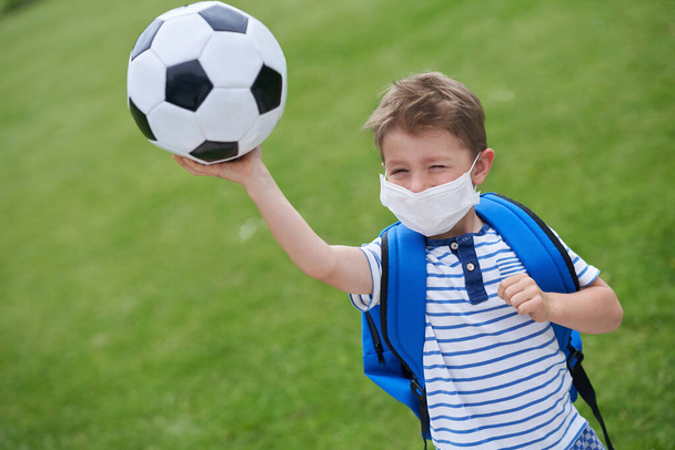 Roztomilý chlapeček s fotbalem a ochrannou maskou na hřišti - Fotografie, Obrázek