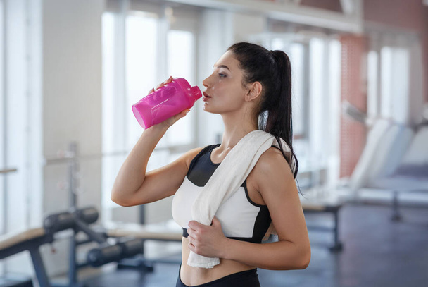 Молодая спортсменка пьет протеиновый коктейль после тренировки в спортивном клубе
 - Фото, изображение