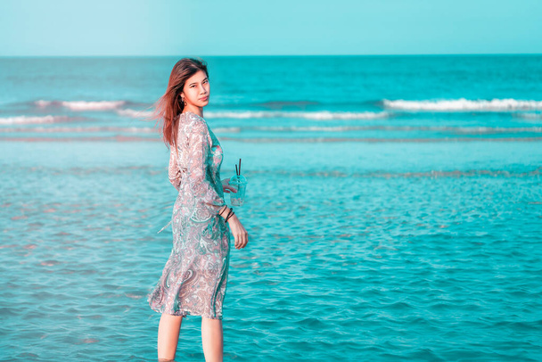 Hermosa mujer asiática joven se relaja en una playa azul de verano para vacaciones de verano Viajes y concepto de moda en tonos azules y naranjas
. - Foto, Imagen