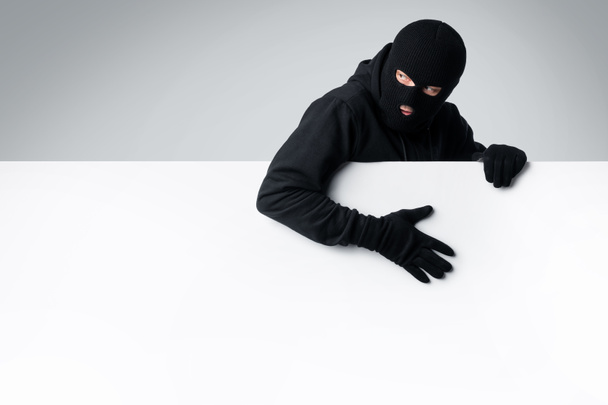 Masked thief holding white blank advertising board - Foto, Imagen