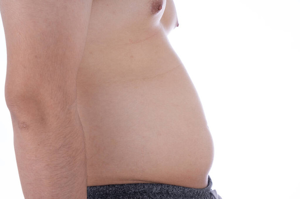 隔離された白い背景の過度の脂肪の腹を閉じます。太りすぎの腹部。人の食事生活様式の概念は腹を減らし、健康な胃の筋肉を形作る。体重減少、スリムなボディコンセプト. - 写真・画像