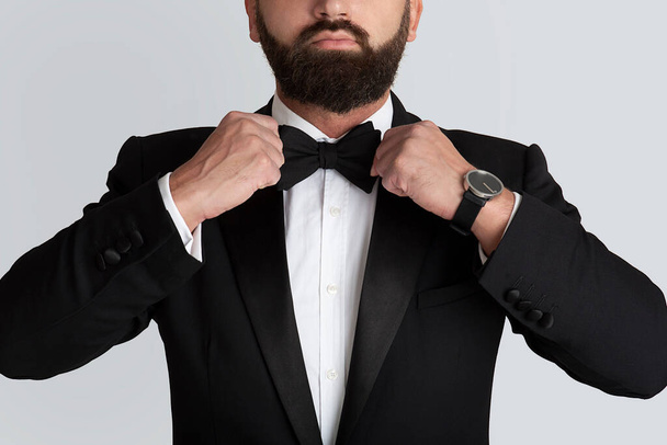 Cropped view of young man in formal suit adjusting bow tie on grey background, closeup - Photo, Image
