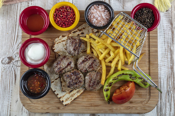 Boulettes de viande turques (Turkish Food Kofte ou Kofta) avec poivrons rouges, tomate, frites et oignon sur une planche à découper en bois. - Photo, image