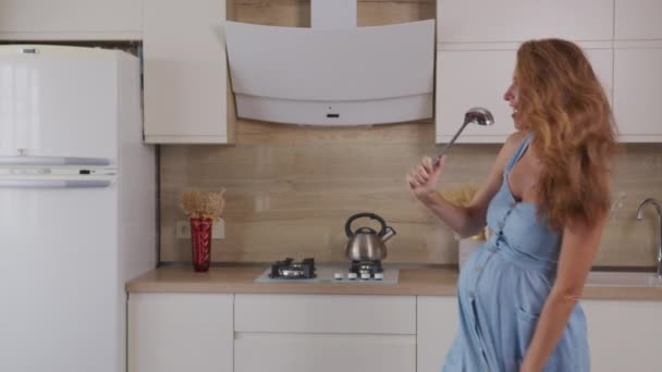 Mama w ciąży słucha muzyki i tańczy w domu w kuchni. Portret Kobieta stojąca w kuchni Słoneczny dzień. - Materiał filmowy, wideo