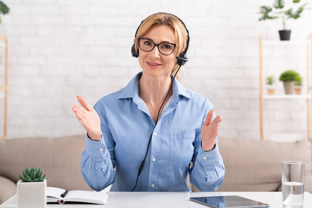 Bizneswoman rozmawia z klientem online. Kobieta z słuchawkami gestykulacji do kamery - Zdjęcie, obraz