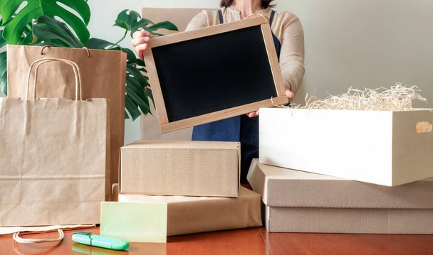 クラフト紙のバッグやボックスの多くは、通知ボードとPackerの近くに滞在します。顧客のための統一梱包注文の配達サービスの労働者. - 写真・画像