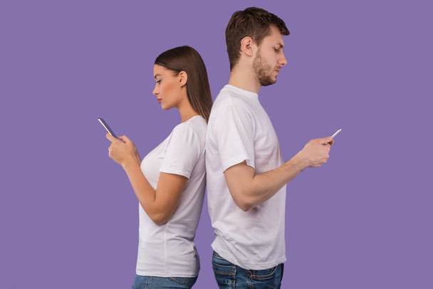 Portrét mladého páru stojící zády k sobě pomocí telefonů - Fotografie, Obrázek