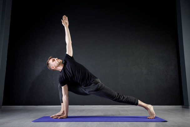 Młody człowiek ćwiczący rozciąganie nóg na macie do jogi na siłowni. Ćwiczenie pozycji jogi. - Zdjęcie, obraz