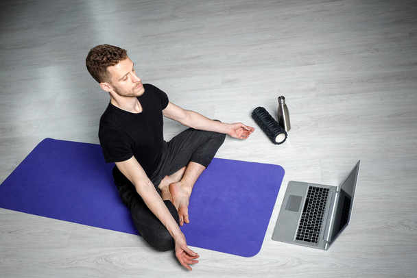 Молодой спортсмен медитирует перед ноутбуком. Уроки йоги онлайн
. - Фото, изображение