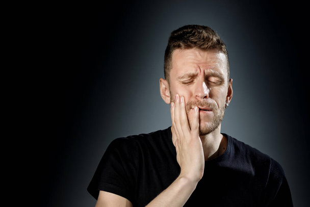 Молодий чоловік, показуючи біль, відчуття зубного болю на чорному тлі
. - Фото, зображення