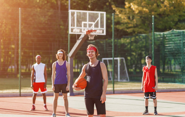 Esportista caucasiano segurando bola com sua equipe diversificada na arena de basquete ao ar livre
 - Foto, Imagem