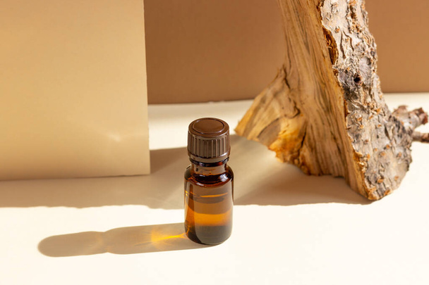 Glass cosmetic bottles with a dropper stand next to a log on a beige background with bright sunlight. The concept of natural cosmetics, natural essential oil - Foto, Imagem