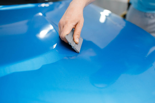 Automobilový obal, mechanik s těsněním instaluje ochrannou vinylovou fólii nebo fólii na kapotu vozidla. Dělník dělá autodílny. Ochranná vrstva automobilových nátěrů, profesionální ladění - Fotografie, Obrázek