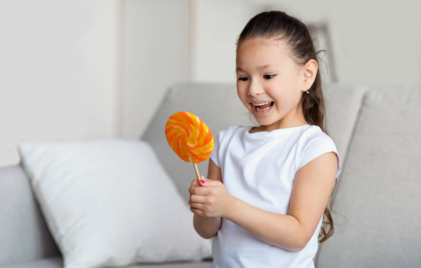 Šťastná asijská dívka drží velké lízátko sladkosti stojící doma - Fotografie, Obrázek