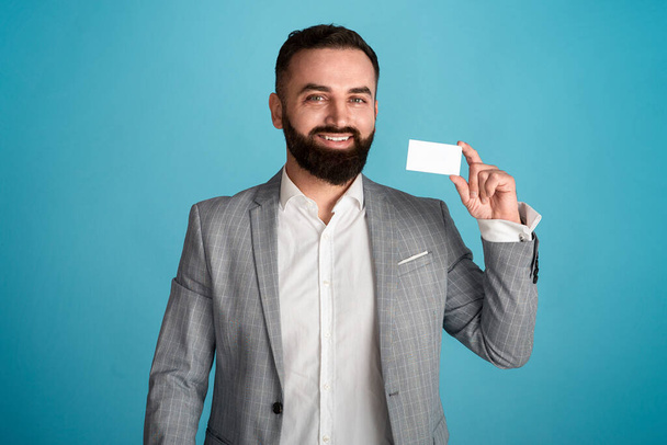 Πορτρέτο του χαρούμενου επιχειρηματία δείχνει επαγγελματική κάρτα με κενό χώρο για το σχεδιασμό σε μπλε φόντο - Φωτογραφία, εικόνα