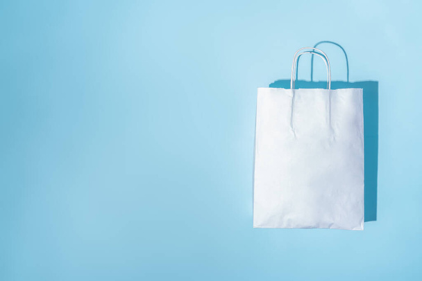 Shopping paper bag. Concept of consumerism, shopping symbol. Copy space trend pastel color. Hard shadows, morning light. - 写真・画像