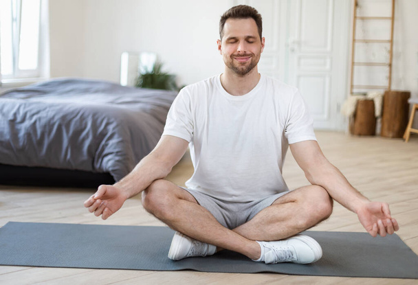 Homem meditando sentado na posição de lótus relaxando em casa
 - Foto, Imagem