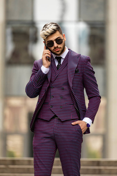 a business man talks on his cell phone as he walks down stairs. Man wearing at violet luxery three-piece suit - Фото, изображение