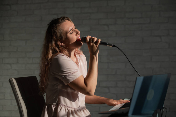 Expressive female singer has a video blog on a laptop. Portrait of a girl recording a song on a web camera and composing on a synthesizer. Online music lessons. Distance learning in quarantine. - Фото, изображение