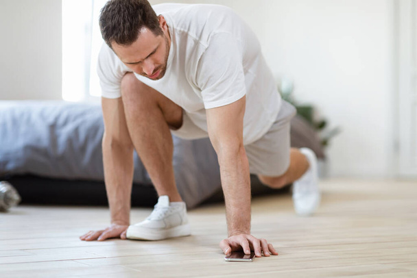 Man Turning On Timer On Smartphone Doing Lunge Exercise Indoor - Foto, Bild