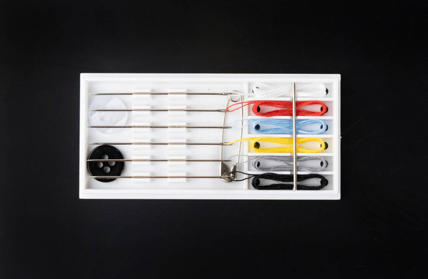 Pequeno kit de costura com agulhas, fios multicoloridos, pinos e botões. Kit de viagem de costura ou caixa de hotel no fundo preto vista superior
 - Foto, Imagem