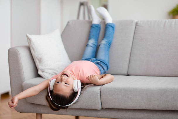 Chica escuchando música divirtiéndose sentado boca abajo en el sofá en interiores
 - Foto, imagen