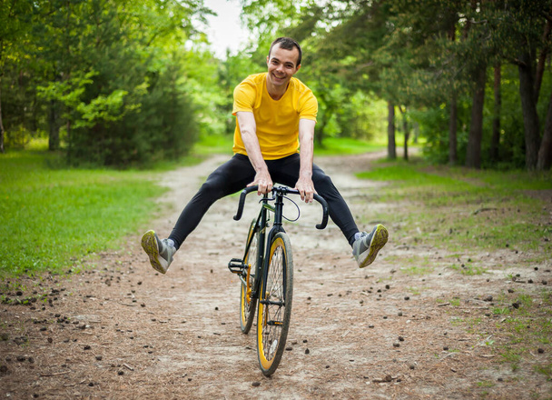 Portret młodego człowieka poruszającego się na rowerze. W parku publicznym, wśród drzew i roślinności. - Zdjęcie, obraz