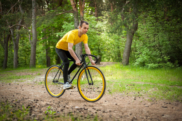 Bisiklete binen genç bir adamın portresi. Halk parkında, ağaçların ve bitkilerin arasında.. - Fotoğraf, Görsel