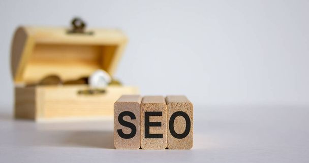Concept word SEO on blocks on a beautiful white background, small chest with coins. - 写真・画像