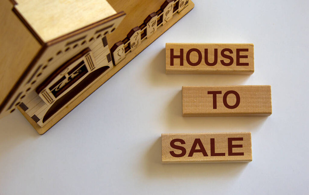 Wooden blocks form the words 'house to sale' near miniature house. Beautiful white background, copy space. - Zdjęcie, obraz