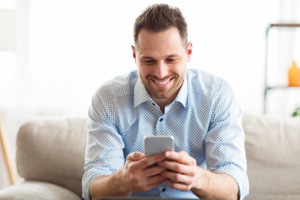 Cheerful adult man using smart phone at home - Foto, afbeelding