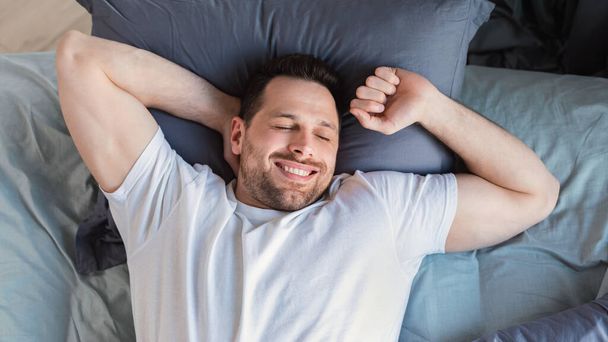 Happy Guy se réveillant allongé au lit à la maison, vue sur le dessus - Photo, image
