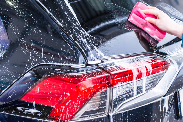 Girl cleaning automobile with sponge at car wash, car washing - Foto, imagen
