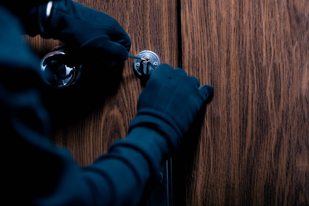 Räuber mit schwarzer Maske knackt Tür mit Metallschlüssel - Foto, Bild