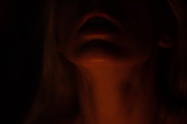 los labios y el cuello de la barbilla están iluminados por una vela sobre un fondo oscuro
 - Foto, imagen