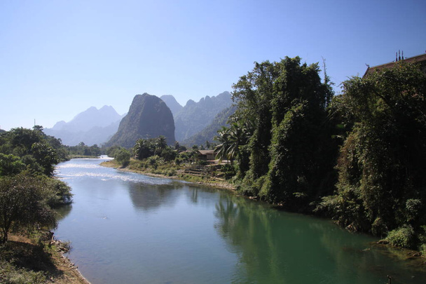 Panoramic scenic view of Nam Song (Xong) river amidst trees and rural karst hills landscape against blue clear sky , near Vang Vieng, Laos - Foto, Bild