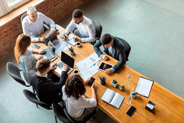 Πολυφυλετική επιχειρηματική ομάδα εργασίας κάθεται στο τραπέζι στο γραφείο, υψηλής γωνίας - Φωτογραφία, εικόνα