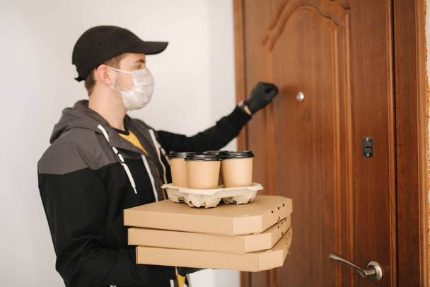 Uomo consegna pizza e caffè al cliente in maschera e guanti. Tema di Coronavirus. Uomo che bussa alle porte
 - Foto, immagini