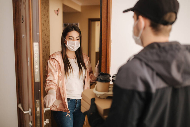 Mann liefert Kunden in Maske und Handschuhen Pizza und Kaffee. Frau öffnet Tür und Ordnung. Coronavirus-Thema - Foto, Bild
