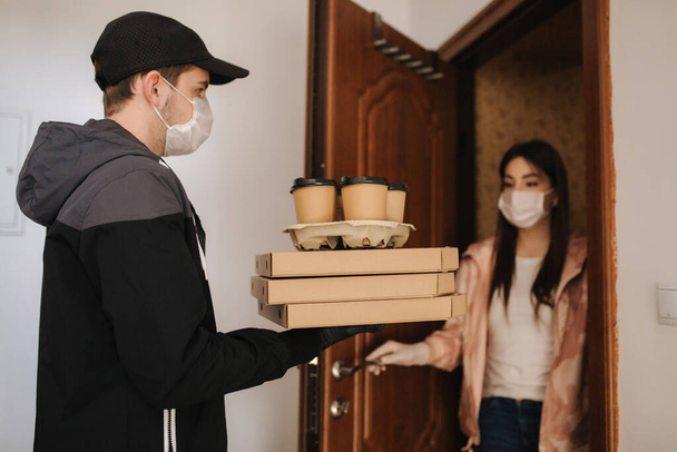 Man delivery pizza and coffe to customer in mask and gloves. Woman open door and take order. Coronavirus theme - Foto, imagen